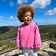 Elayana a rejoint le concours — aidez-le/la à gagner de superbes lots ! blue_sky, child, clouds, curly_hair, daylight, happy, hills, map_display, nature, outdoor, person, pink_sweater, portrait, railing, smiling, standing, stone_wall, sunny, toddler, white_pants