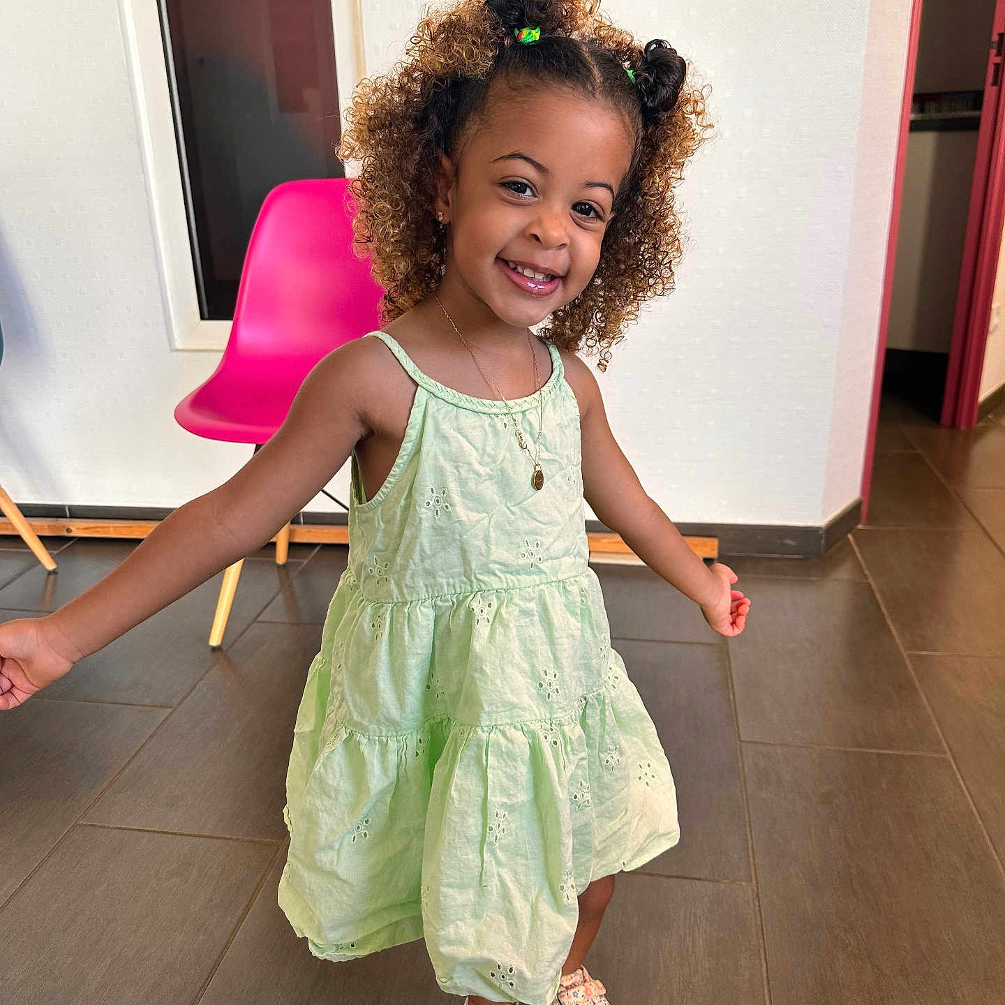 Elayana participe au concours pour gagner de l'argent avec cette photo : chair, child, curly_hair, cute, dress, floor, floral_sneakers, girl, green_dress, happy, indoor, jewelry, necklace, person, pink_chair, playful, smiling, sneakers, standing, tile_floor