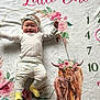Brixlee is registered to the contest to win money with this photo: baby, infant, smiling, headband, pants, socks, blanket, floral, numbers, milestone, highland_cows, painting, cute, baby_clothes, happy, lying_down, child, indoors, portrait, celebration
