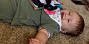Brixlee is registered to the contest to win money with this photo: baby, child, smiling, carpet, green_outfit, bib, soft_book, lying_down, infant, indoors, cute, happy, skin, person, head, hand, toy, floor, expression, closeup