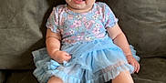 Brixlee joined the competition — help win amazing prizes! baby, child, tutu, pink_bow, headband, couch, green_couch, smiling, happy, curly_hair, floral_top, blue_skirt, sitting, barefoot, indoor, cute, infant, person, clothing, portrait