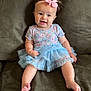 baby, child, tutu, pink_bow, headband, couch, green_couch, smiling, happy, curly_hair, floral_top, blue_skirt, sitting, barefoot, indoor, cute, infant, person, clothing, portrait