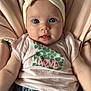 baby, infant, headband, bow, pink_shirt, clover, love_text, blue_eyes, denim_pants, soft_cushion, seated, cute, adorable, portrait, child, clothing, face, expression, curious, indoor