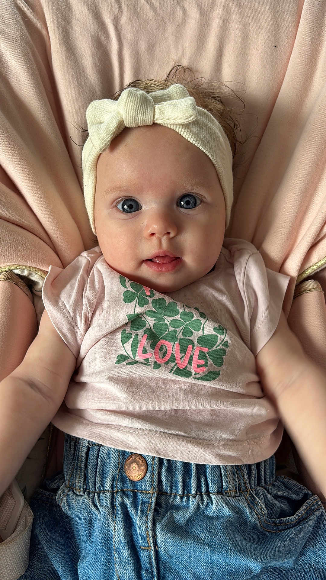 Thays a rejoint le concours — aidez-le/la à gagner de superbes lots ! baby, infant, headband, bow, pink_shirt, clover, love_text, blue_eyes, denim_pants, soft_cushion, seated, cute, adorable, portrait, child, clothing, face, expression, curious, indoor