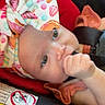 baby, infant, car_seat, headband, colorful, orange_clothing, safety_warning, thumb_sucking, cute, child, face, eyes, seatbelt, warning_label, fabric, soft, comfort, portrait, closeup, indoors