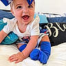 baby, child, smiling, blue_bow, white_clothing, blue_socks, bed, pillow, blanket, happy, crawling, indoors, cute, infant, portrait, person, headwear, fabric, soft, comfort