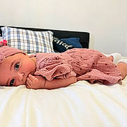 Adaline is registered to the contest to win money with this photo: baby, infant, child, bed, pillow, blanket, headband, pink_clothing, socks, indoor, sleepwear, person, cute, lying_down, hand, face, eyes, soft, cozy, room