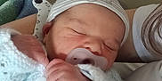 Eren participe au concours pour gagner de l'argent avec cette photo : newborn, baby, sleeping, pacifier, knitted_sweater, hat, hospital_bed, blanket, person, hand, infant, cozy, cute, resting, indoor, closeup, soft, peaceful, care, parent