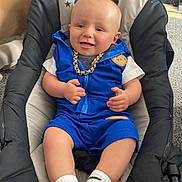 Tommy is registered to the contest to win money with this photo: baby, baby_seat, blue_outfit, carpet, cat_tail, child, clothing, cushion, cute, footwear, furniture, gold_chain, happy, head, indoor, living_room, person, portrait, smiling, white_socks