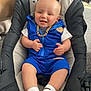 Tommy is registered to the contest to win money with this photo: baby, baby_seat, blue_outfit, carpet, cat_tail, child, clothing, cushion, cute, footwear, furniture, gold_chain, happy, head, indoor, living_room, person, portrait, smiling, white_socks