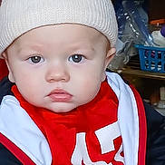 Malachi joined the competition — help win amazing prizes! baby, child, hat, knit_hat, red_clothing, white_clothing, person, face, hand, elderly_person, arm, indoors, portrait, expressionless, closeup, warm_clothing, pom_pom, seated, human, generations