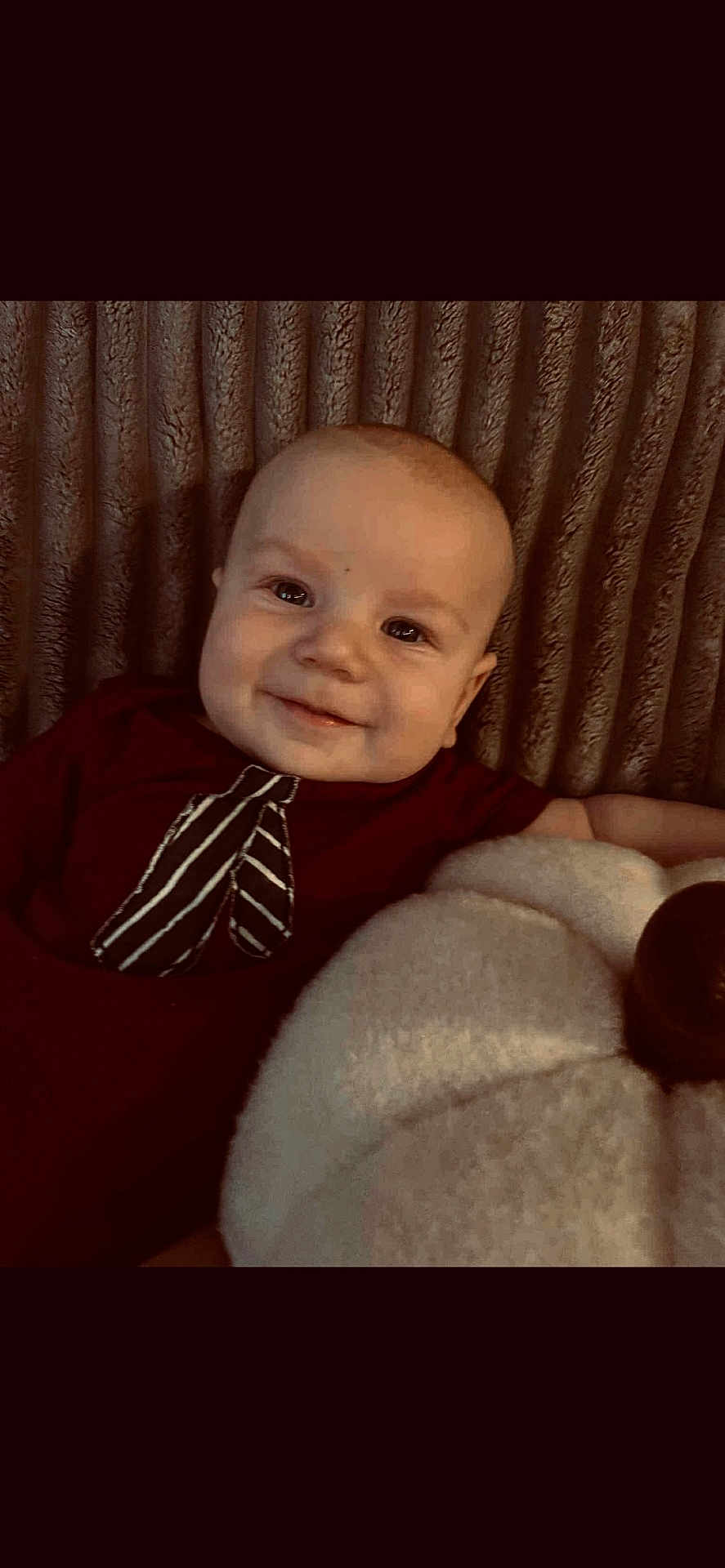 Walker is registered to the contest to win money with this photo: baby, smiling, infant, portrait, indoors, plush, pumpkin, maroon_clothing, tie_design, texture, comfort, child, face, happy, cute, cozy, background, soft, young, lying_down