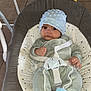 baby, baby_boy, baby_clothing, baby_rocker, baby_seat, blue_booties, child, comfort, cushion, face, feet, hands, hat, indoor, infant, onesie, seated, small_person, straps, tile_floor