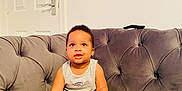 Kayce joined the competition — help win amazing prizes! toddler, child, baby, couch, gray_couch, plush, indoor, tank_top, red_shorts, plaid, barefoot, cute, sitting, curious, young_child, home_interior, door, wall, light_switch, relaxed