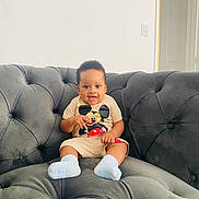 Kayce joined the competition — help win amazing prizes! baby, child, smiling, mickey_mouse, tshirt, socks, couch, sofa, tufted, gray, indoor, happy, seated, furniture, person, home, cute, infant, young_child, casual