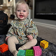 Lily is registered to the contest to win money with this photo: baby, child, smiling, sitting, toy_blocks, indoor, carpet, colorful, cute, face, person, clothing, happy, playtime, floor, toddler, home, soft_texture, young_child, portrait