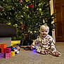 baby, child, christmas_tree, pajamas, carpet, toys, blocks, doll, holiday, decorations, indoors, smiling, festive, lights, ornaments, wooden_door, couch, floor, cute, infant