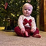 Lily is registered to the contest to win money with this photo: baby, child, christmas_tree, holiday, carpet, indoor, sweater, red_bow, red_pants, blond_hair, cute, festive, decorations, lights, holiday_season, portrait, sitting, cozy, smiling, face