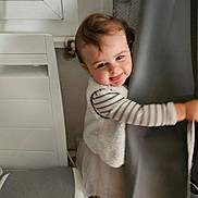 Lina a rejoint le concours — aidez-le/la à gagner de superbes lots ! toddler, child, indoor, curtain, chair, striped_shirt, vest, skirt, playful, smiling, pigtails, hair, floor, window, wall, person, footwear, cute, hugging, home