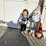 Lina participe au concours pour gagner de l'argent avec cette photo : toddler, child, pacifier, plush_toy, owl, gnome, hat, jacket, shoes, door, shadow, sunlight, outdoor, concrete, curly_hair, standing, wall, playful, cute, person