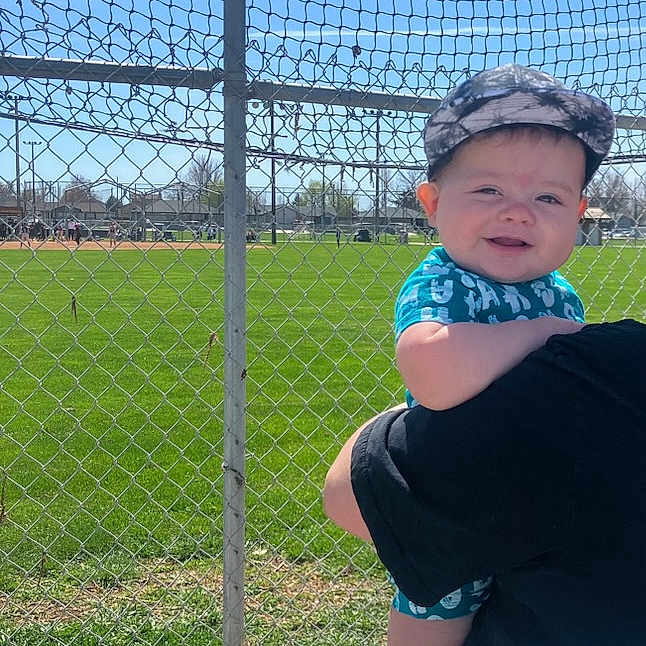 Ryder is registered to the contest to win money with this photo: baby, baseballcap, cap, clothing, face, fence, glove, grass, hat, head, nature, outdoors, pants, park, people, person, photography, plant, portrait, t_shirt