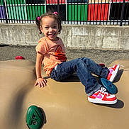 Harmony joined the competition — help win amazing prizes! child, smiling, playground, climbing_structure, sneakers, pink_hair_ties, orange_shirt, jeans, outdoor, sunny, fence, colorful_wall, concrete, happy, person, young, casual_clothing, daylight, recreation, play