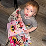 toddler, child, blue_eyes, curious, floor, wooden_floor, book, activity_book, minnie_mouse, red, chair, black, indoor, casual_clothing, short_hair, person, play, reading, toy, candid