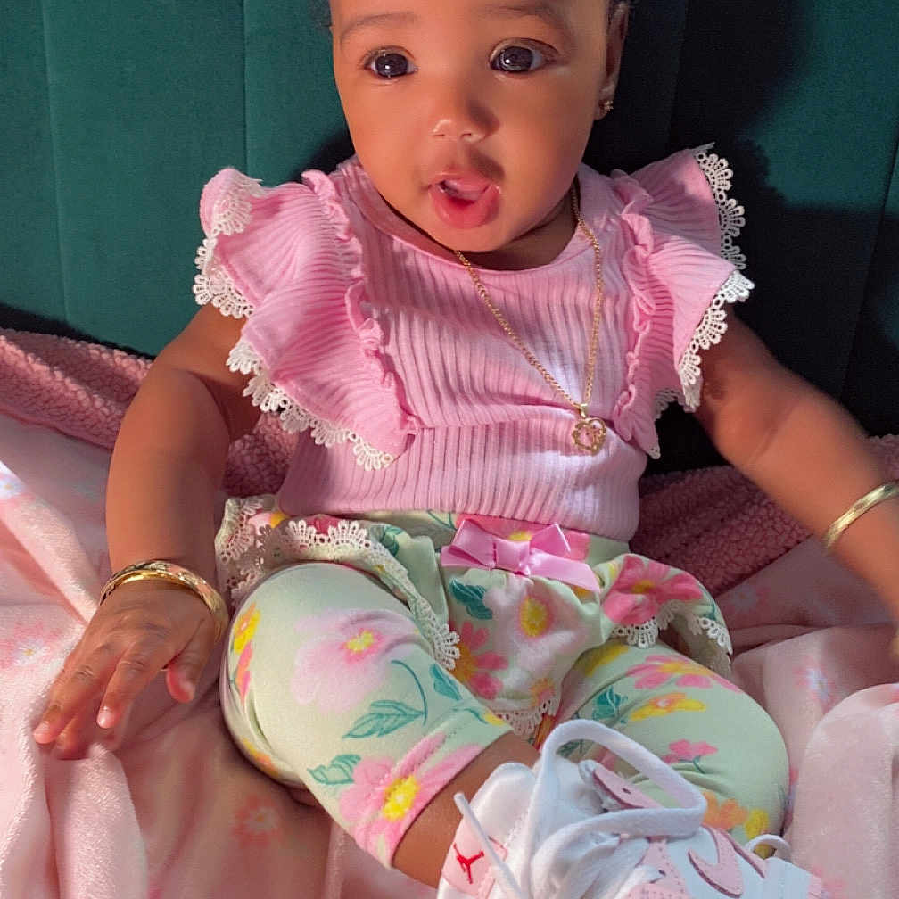 Teiaurie is registered to the contest to win money with this photo: baby, child, pink_clothing, floral_leggings, sneakers, headband, bracelet, blanket, seated, cute, indoors, portrait, jewelry, expression, soft_texture, footwear, fashion, adorable, infant, happy