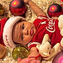 Amani is registered to the contest to win money with this photo: baby, infant, child, santa_hat, christmas_ornament, bauble, plush_toy, stuffed_animal, red_shirt, coca_cola_logo, portrait, closeup, blue_eyes, blanket, soft_texture, holiday_theme, festive, bokeh, toy, calm_expression