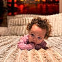 baby, infant, child, curly_hair, blue_eyes, teething, hand_in_mouth, pink_clothes, blanket, bed, lying_down, cozy, soft_texture, bokeh, portrait, indoor, home, background_painting, cute, adorable