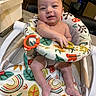 Sebastian is registered to the contest to win money with this photo: baby, infant, child, smiling, portrait, high_chair, indoor, toy, toy_rings, seated, face, hands, bare_arms, colorful, patterned, kitchen, home, furniture, happy, candid