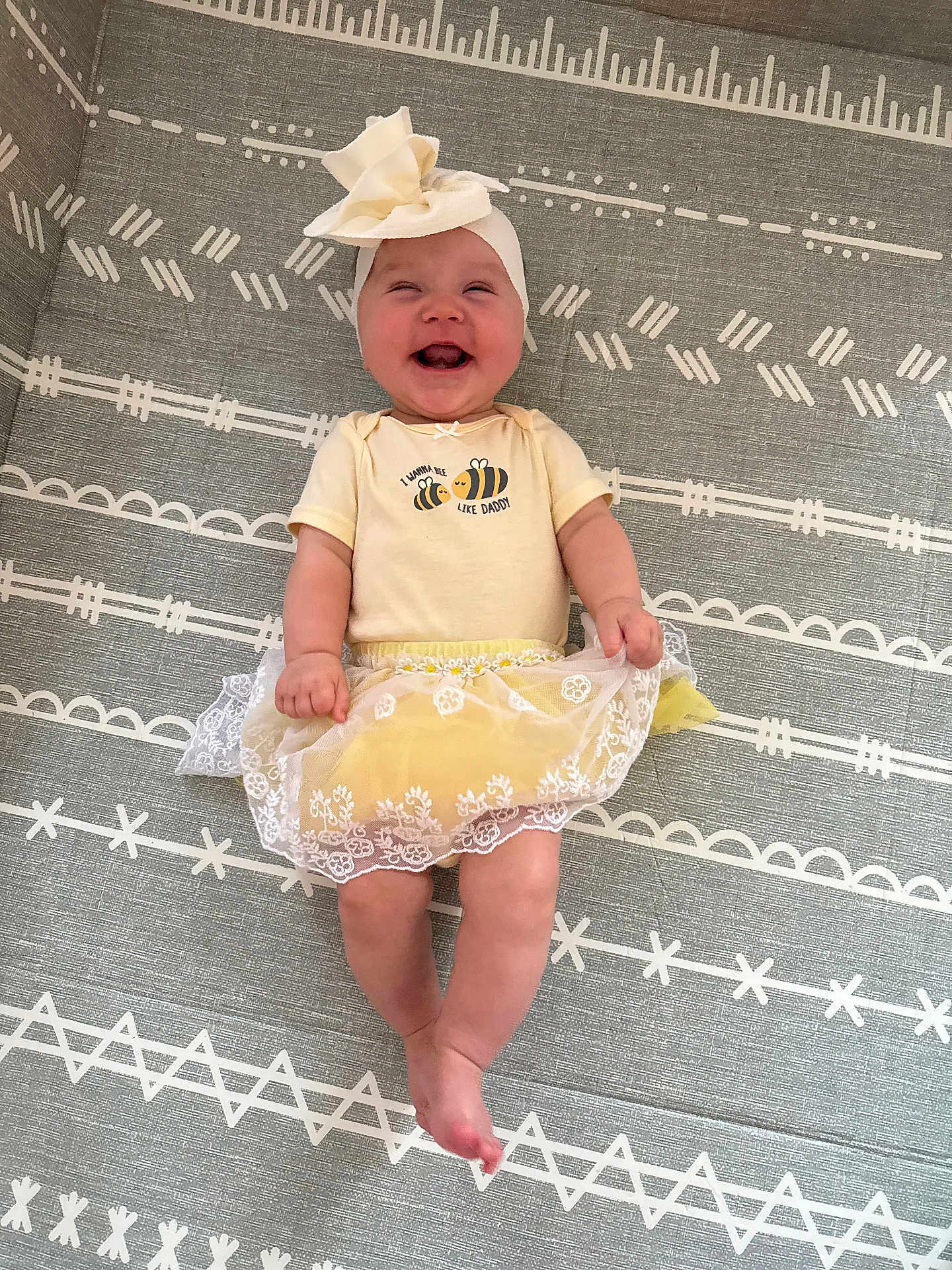 Adalynn joined the competition — help win amazing prizes! baby, smiling, child, yellow_outfit, headband, bow, lying_down, patterned_mat, happy, cute, infant, clothing, indoors, toddler, legs, hands, face, baby_girl, white_lace, joy