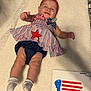 Adalynn is registered to the contest to win money with this photo: baby, infant, smiling, headband, red_flower, dress, striped_clothing, blue_shorts, socks, blanket, footprint_art, handprint_art, american_flag, red, white, blue, celebration, patriotic, soft_texture, lying_down