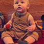 baby, buttoned_shirt, carpet, casual_clothing, child, curious, face, footwear, home_decor, indoor, light, moawk, person, plush_toy, red_carpet, shorts, sitting, snack, toy, wooden_panel