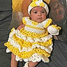 baby, infant, crocheted_clothing, yellow, white, hat, mittens, booties, couch, pillow, portrait, indoors, cute, child, knitwear, handmade, relaxed, looking_at_camera, soft_lighting, cozy