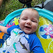 Jace joined the competition — help win amazing prizes! baby, smiling, child, inflatable_pool, swimsuit, shark_pattern, water, outdoor, grass, fan, summer, cute, happy, playtime, infant, blue_clothing, colorful, sunny, relaxed, fun