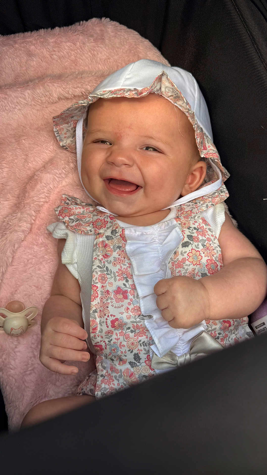 Harlow Rivah is registered to the contest to win money with this photo: baby, smiling, floral_outfit, bonnet, pink_blanket, pacifier, infant, cute, happy, portrait, child, soft_texture, white_clothing, closeup, indoors, hand, face, sitting, cozy, adorable