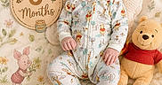 Elora is registered to the contest to win money with this photo: baby, infant, smiling, winnie_the_pooh, plush_toy, pajamas, blanket, wooden_sign, flowers, soft_lighting, cute, child, lying_down, decor, illustration, stuffed_animal, happy, face, footwear, cozy