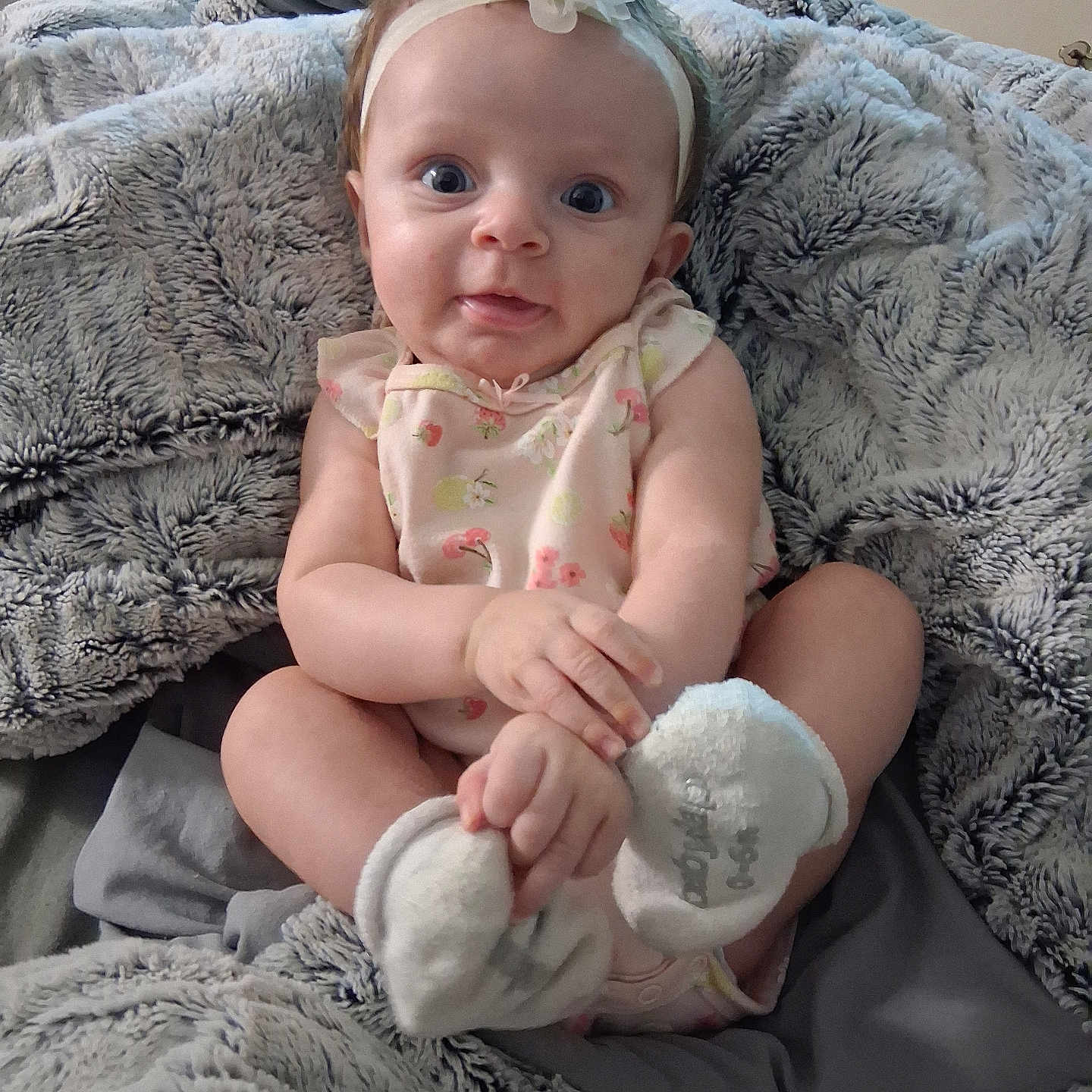 Elora is registered to the contest to win money with this photo: baby, infant, child, onesie, headband, flower, blanket, soft, gray, cute, hands, feet, sitting, indoors, furniture, curious, portrait, person, cozy, expression