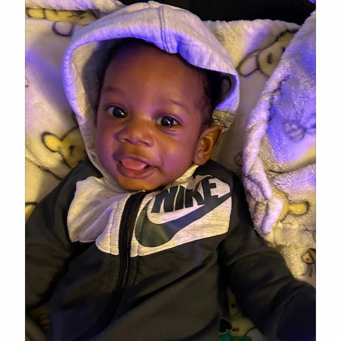 Royal is registered to the contest to win money with this photo: baby, child, hoodie, nike, blanket, smile, tongue_out, cute, infant, clothing, indoors, portrait, happy, cozy, soft, young_child, face, sitting, baby_garment, casual