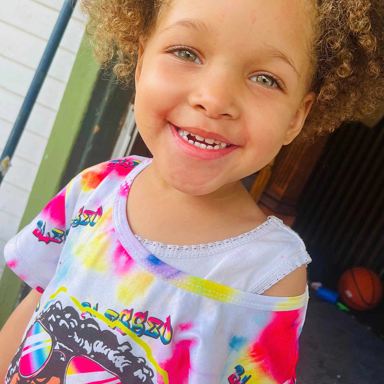 Zahra Harris joined the competition — help win amazing prizes! basketball, casual, child, colorful_clothing, curly_hair, cute, daylight, expression, face, front_view, happy, outdoor, person, playful, portrait, smiling, tie_dye_shirt, toy, tshirt, young