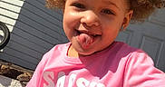 Zahra Harris joined the competition — help win amazing prizes! casual_clothing, child, curly_hair, cute, daylight, earrings, fun, happy, outdoor, person, pigtails, pink_shirt, playful, portrait, sitting, smiling, steps, sunlight, tongue_out, wooden