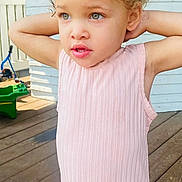 Zahra Harris joined the competition — help win amazing prizes! child, girl, outdoor, dress, pink, curly_hair, deck, wooden_floor, porch, sunlight, standing, person, casual_clothing, hairstyle, young_child, expression, daylight, white_wall, fence, background