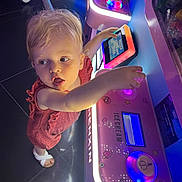 Léna participe au concours pour gagner de l'argent avec cette photo : toddler, child, arcade_machine, pink_dress, white_sandals, neon_lights, indoor, game, curious, playful, technology, floor_tiles, hand, face, young_child, machine, colorful, entertainment, person, light