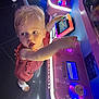 toddler, child, arcade_machine, pink_dress, white_sandals, neon_lights, indoor, game, curious, playful, technology, floor_tiles, hand, face, young_child, machine, colorful, entertainment, person, light