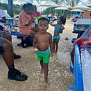 Christopher is registered to the contest to win money with this photo: child, toddler, swimwear, outdoor, summer, picnic, poolside, bench, adult, umbrella, sky, cloud, concrete, footwear, green_shorts, blue_swimsuit, people, sunlight, table, recreation