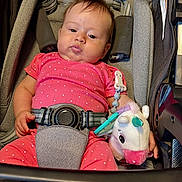 Leah is registered to the contest to win money with this photo: baby, infant, child, car_seat, vehicle,  안전, pink_clothing, polka_dots, seatbelt, buckled, plush_toy, unicorn, pacifier, toy, portrait, indoors, sitting, face, automotive, family
