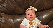 Leah is registered to the contest to win money with this photo: baby, infant, child, portrait, sitting, leather_couch, brown_couch, bow, headband, white_shirt, teddy_bear, denim_shorts, pink_socks, baby_shoes, indoors, living_room, furniture, smiling, centered_subject, casual_clothing
