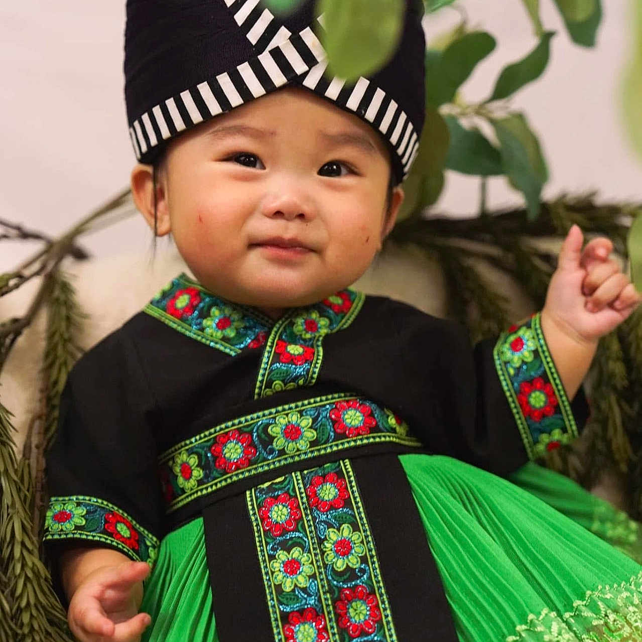 Stella Chang joined the competition — help win amazing prizes! barefoot, branches, child, costume, cute, embroidery, face, floral_pattern, green_dress, hand, happy, hat, indoor, leaves, nature, portrait, smiling, toddler, traditional_clothing, young_child