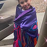child, girl, smiling, purple_shawl, colorful_fringes, car_door, outdoor, grass, rocks, hairstyle, pigtails, sparkle_effect, happy, portrait, clothing, person, daylight, sidewalk, candid, cute